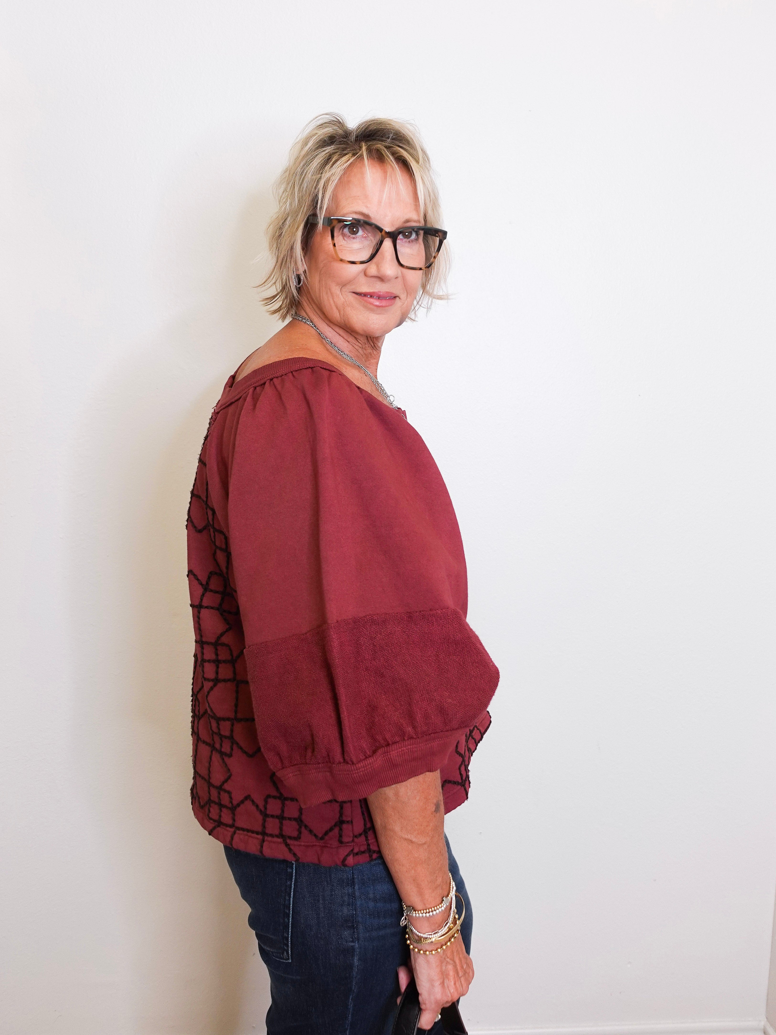 Woman wearing a burgundy blouse with a patterned overlay against a white background