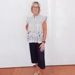 Woman wearing a floral blouse and black pants against a white wall.