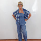 Woman wearing a blue outfit with a patterned top against a white wall.