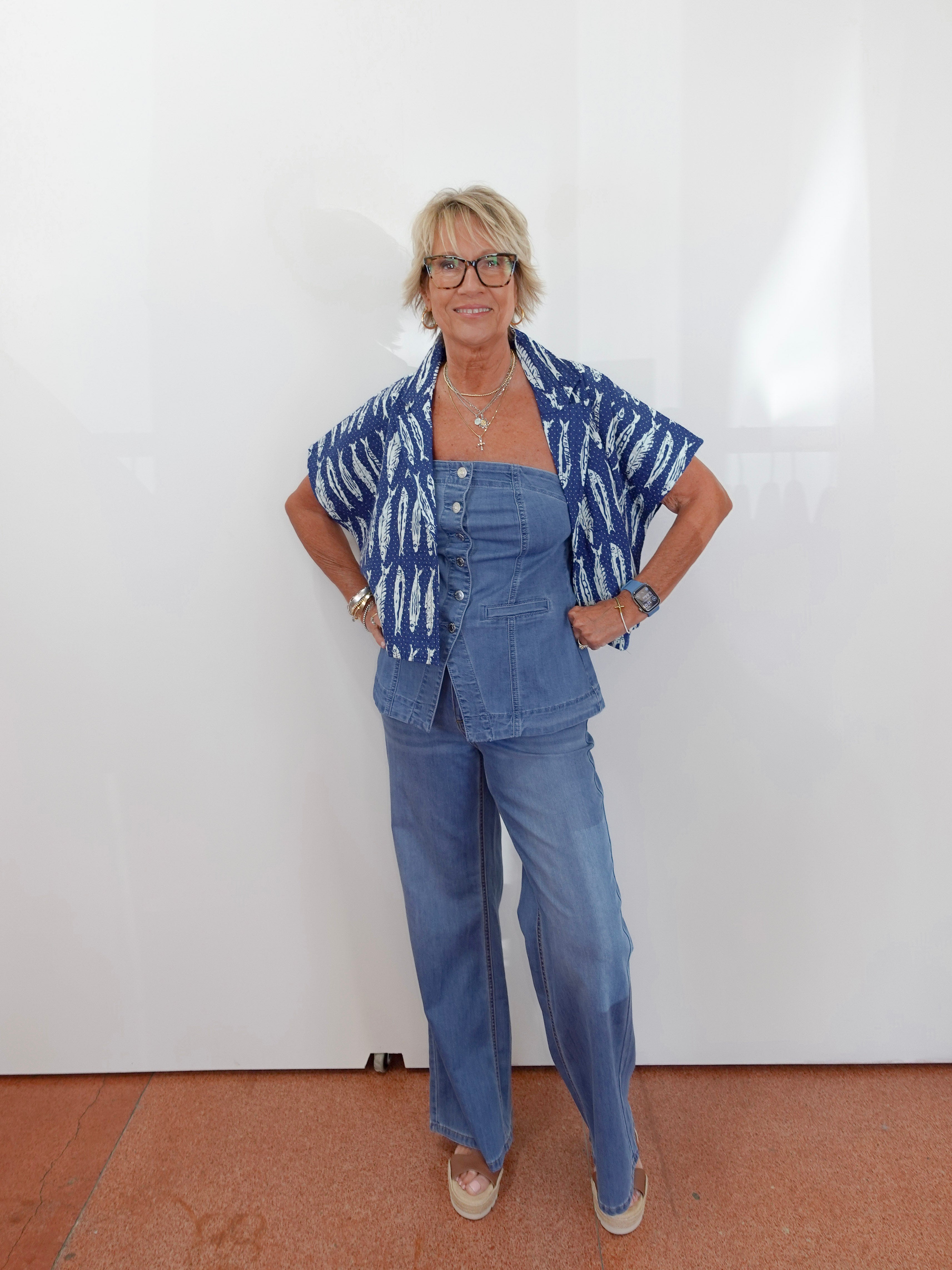 Woman wearing a blue outfit with a patterned top against a white wall.
