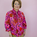Woman wearing a colorful patterned blouse against a pink background