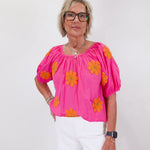 Woman wearing a pink blouse with orange floral patterns on a white background