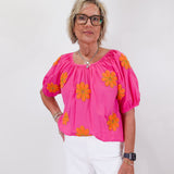 Woman wearing a pink blouse with orange floral patterns on a white background