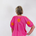Person wearing a bright pink blouse with orange floral patterns on a white background