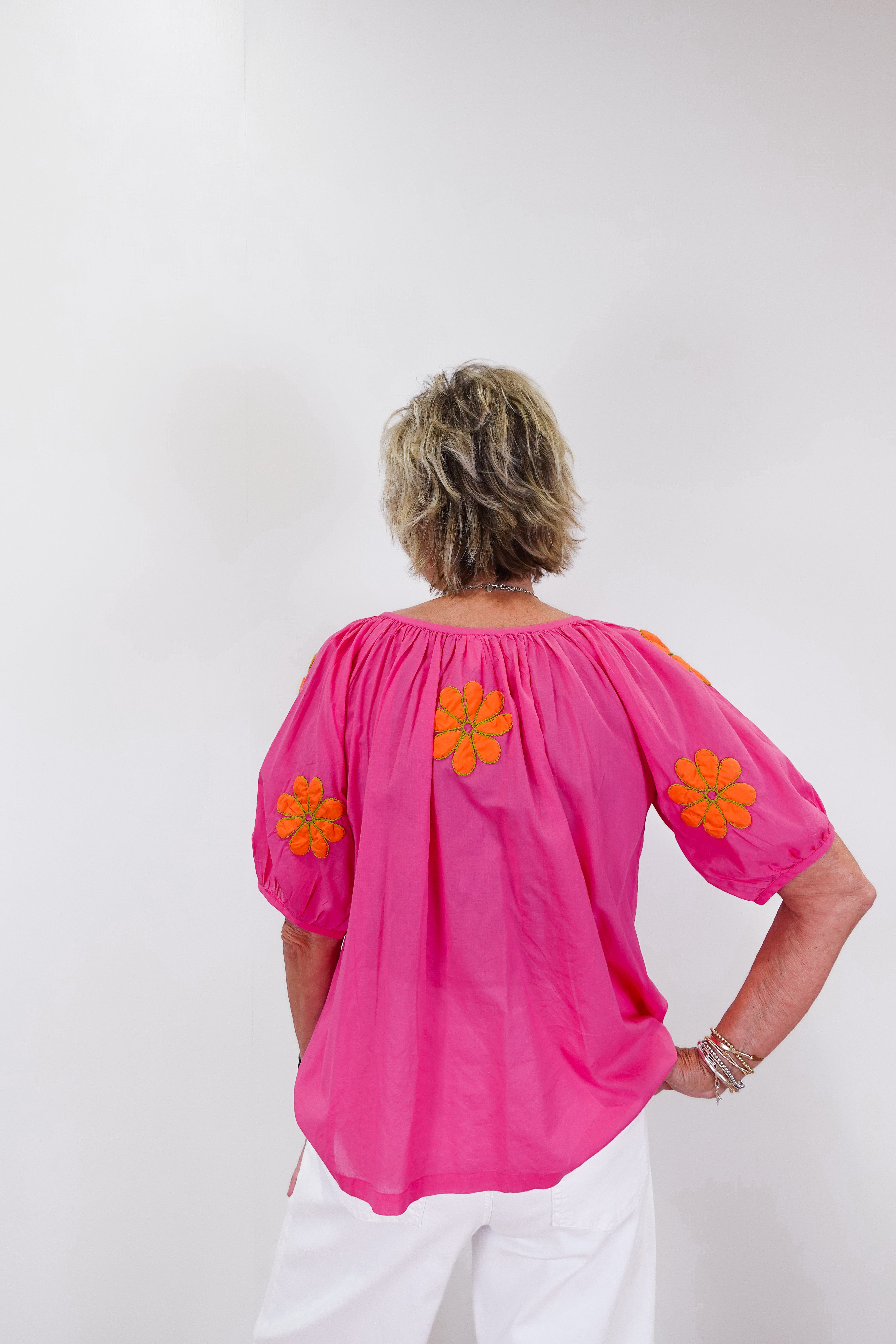 Person wearing a bright pink blouse with orange floral patterns on a white background