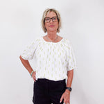 Woman wearing a white blouse with a pattern and black shorts on a white background