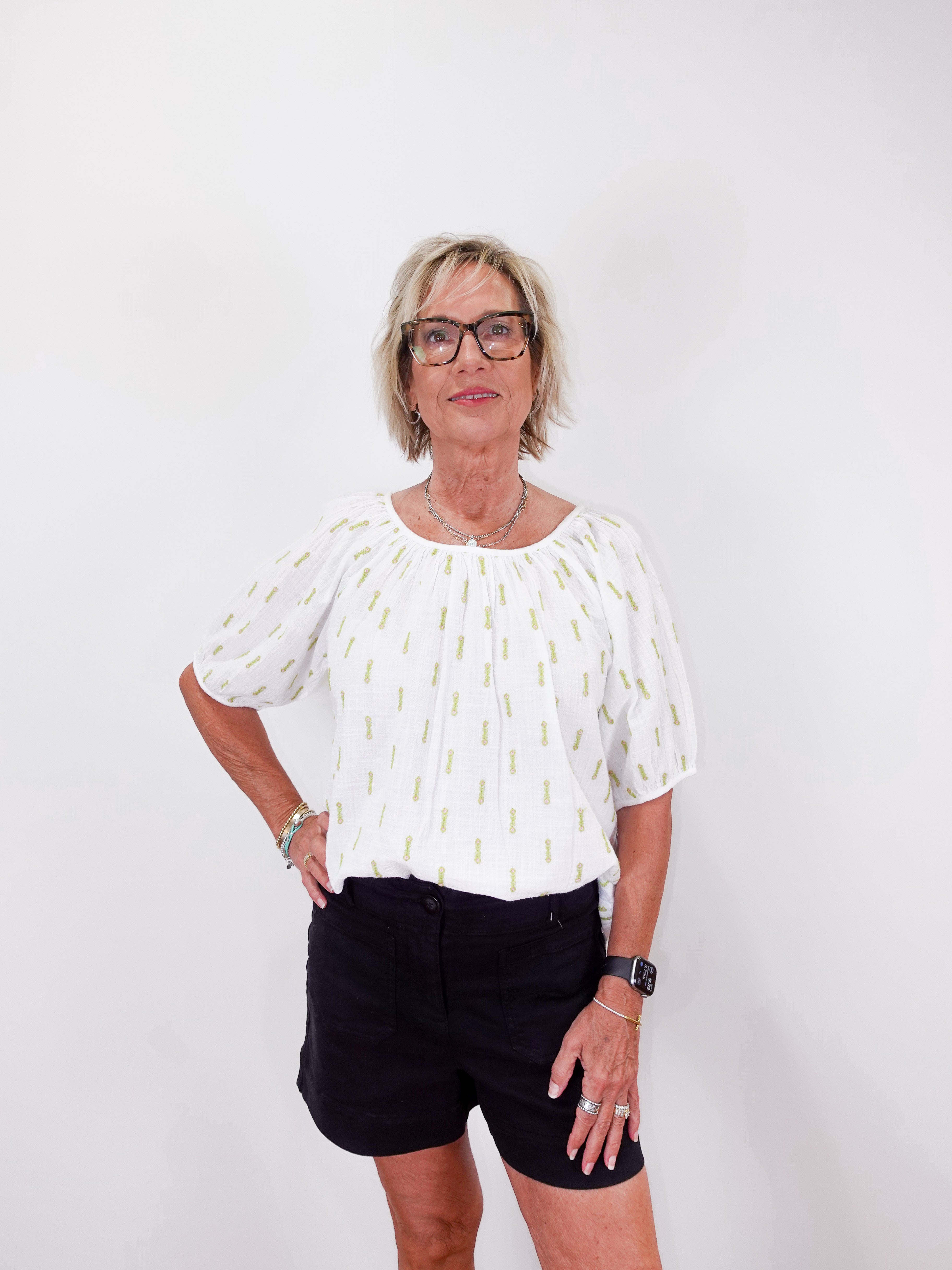 Woman wearing a white blouse with a pattern and black shorts on a white background