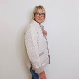 Person wearing a white quilted jacket and blue jeans against a plain background
