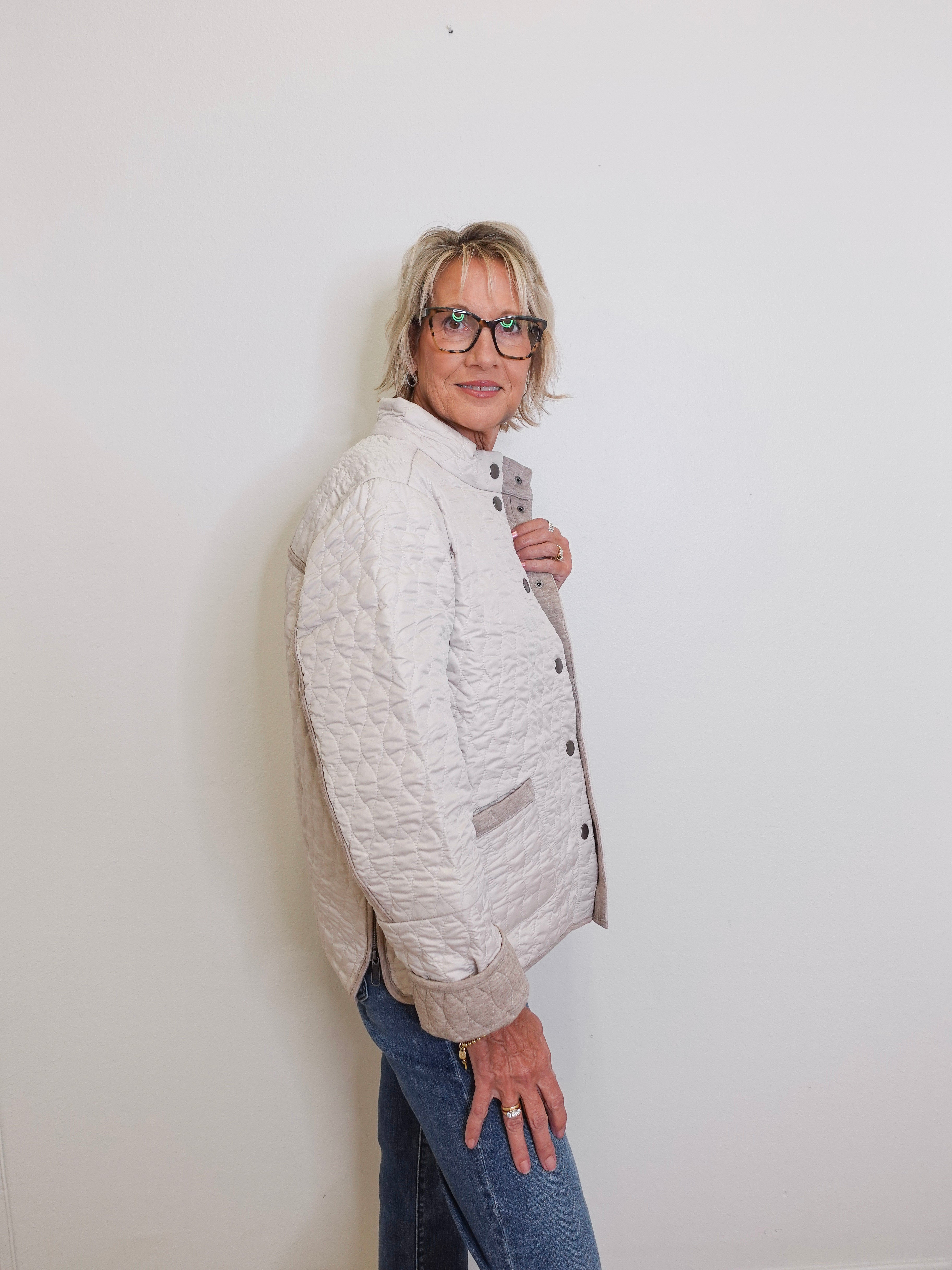 Person wearing a white quilted jacket and blue jeans against a plain background