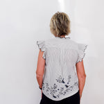 Person wearing a light gray blouse with floral embroidery on a white background