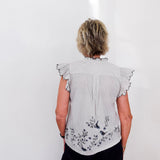 Person wearing a light gray blouse with floral embroidery on a white background