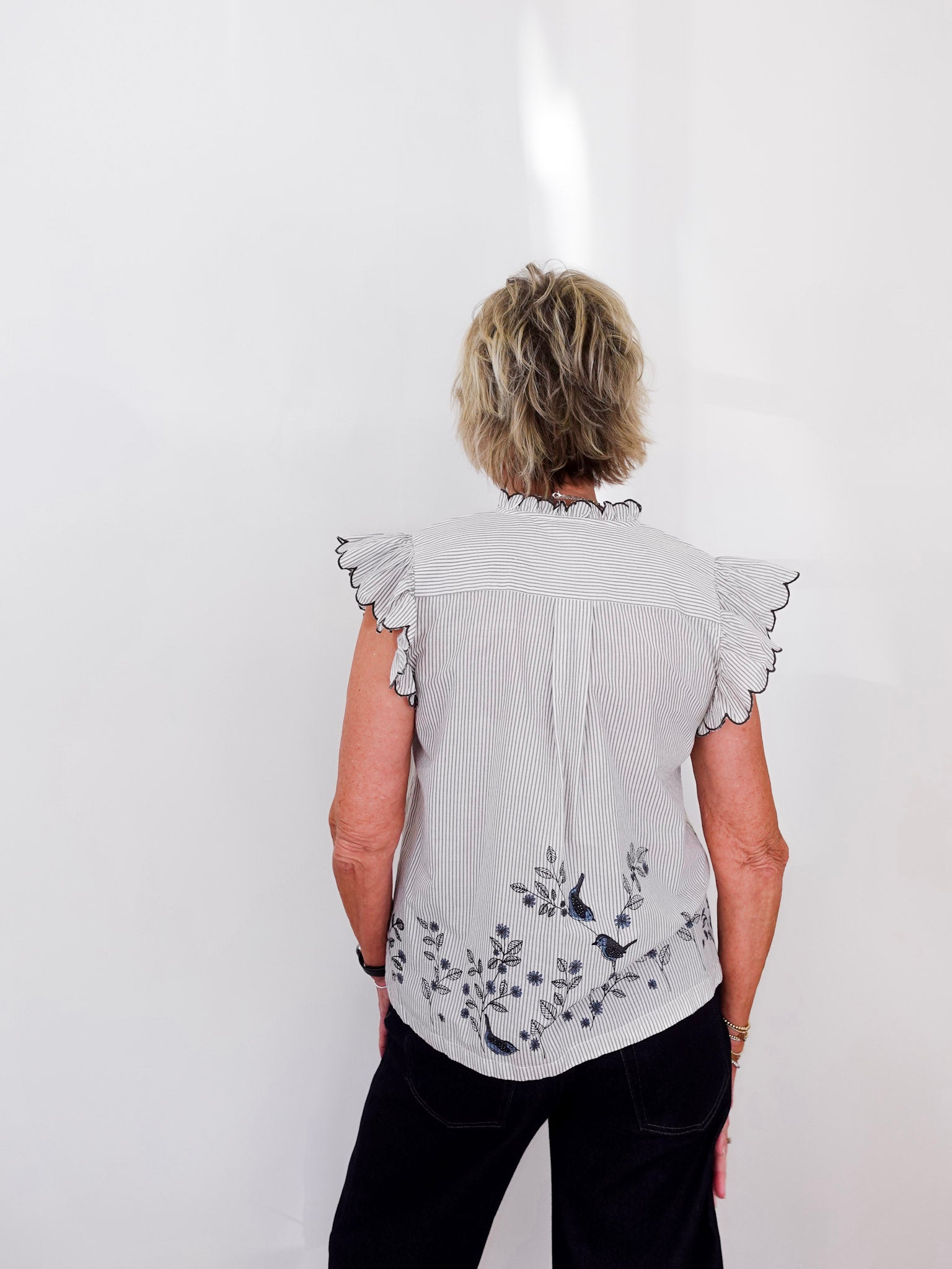 Person wearing a light gray blouse with floral embroidery on a white background