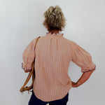 Person wearing a striped shirt and holding a bag against a plain background