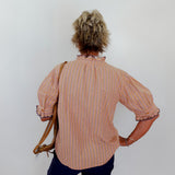 Person wearing a striped shirt and holding a bag against a plain background
