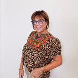 Woman wearing a leopard print top with colorful embroidery against a white background