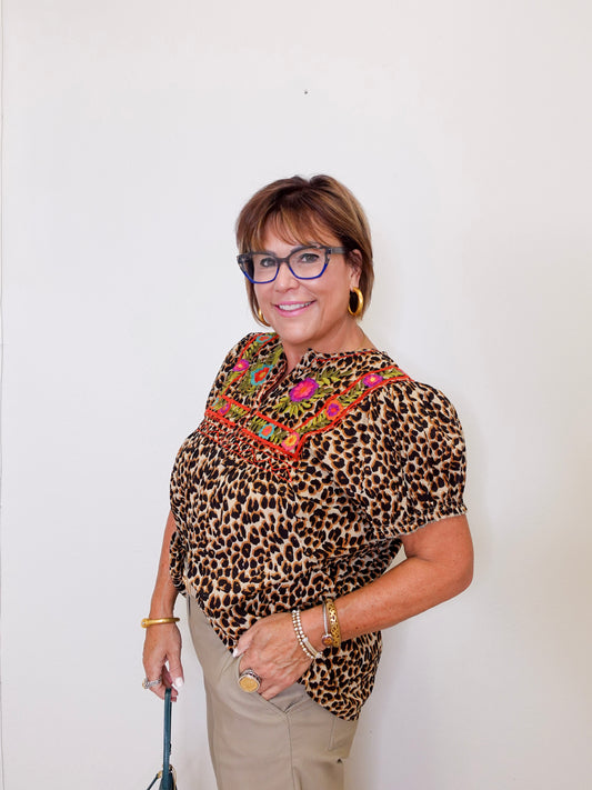 Woman wearing a leopard print top with colorful embroidery against a white background