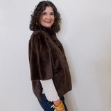 Woman wearing a brown jacket over a white shirt with a plain background