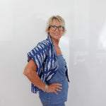 Woman wearing a blue patterned top and jeans against a white background