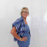 Woman wearing a blue patterned top and jeans against a white background