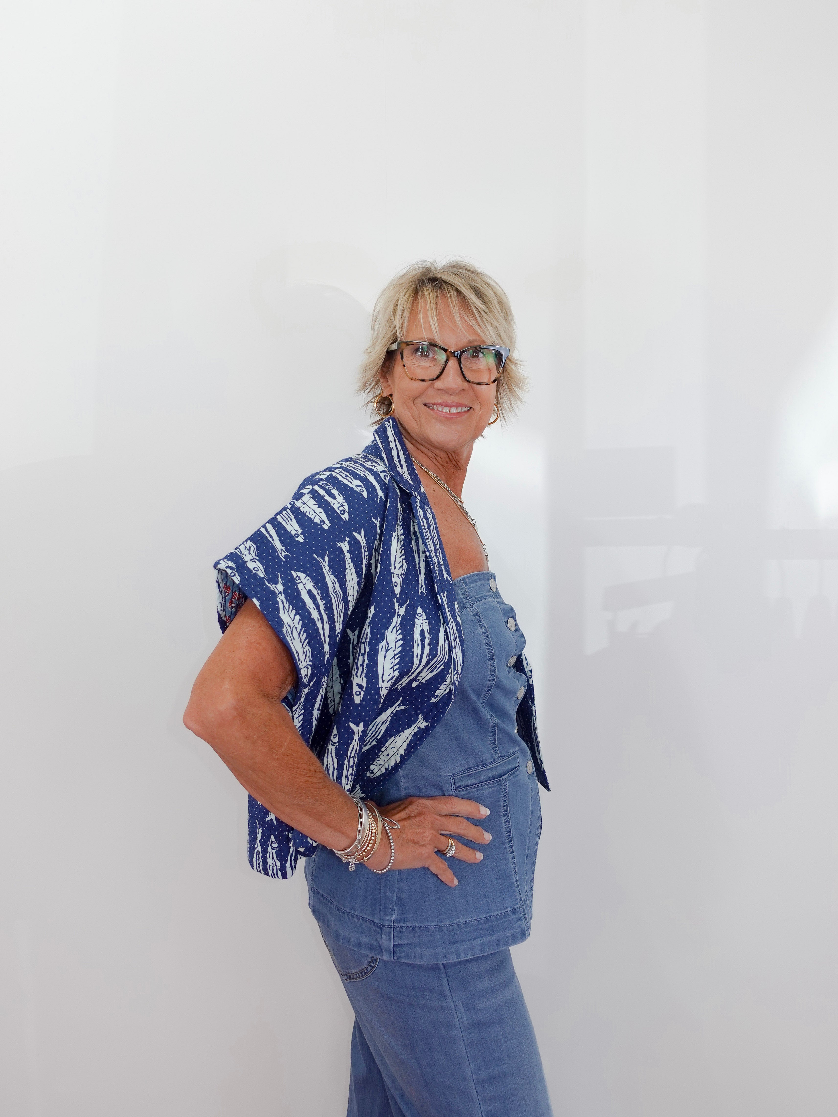 Woman wearing a blue patterned top and jeans against a white background