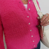 Person wearing a bright pink textured cardigan with buttons, holding a beige handbag.
