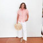Woman wearing a striped shirt and white pants, holding a hat indoors.
