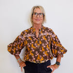 Woman wearing a patterned blouse and black pants against a white background