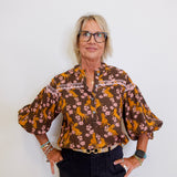 Woman wearing a patterned blouse and black pants against a white background