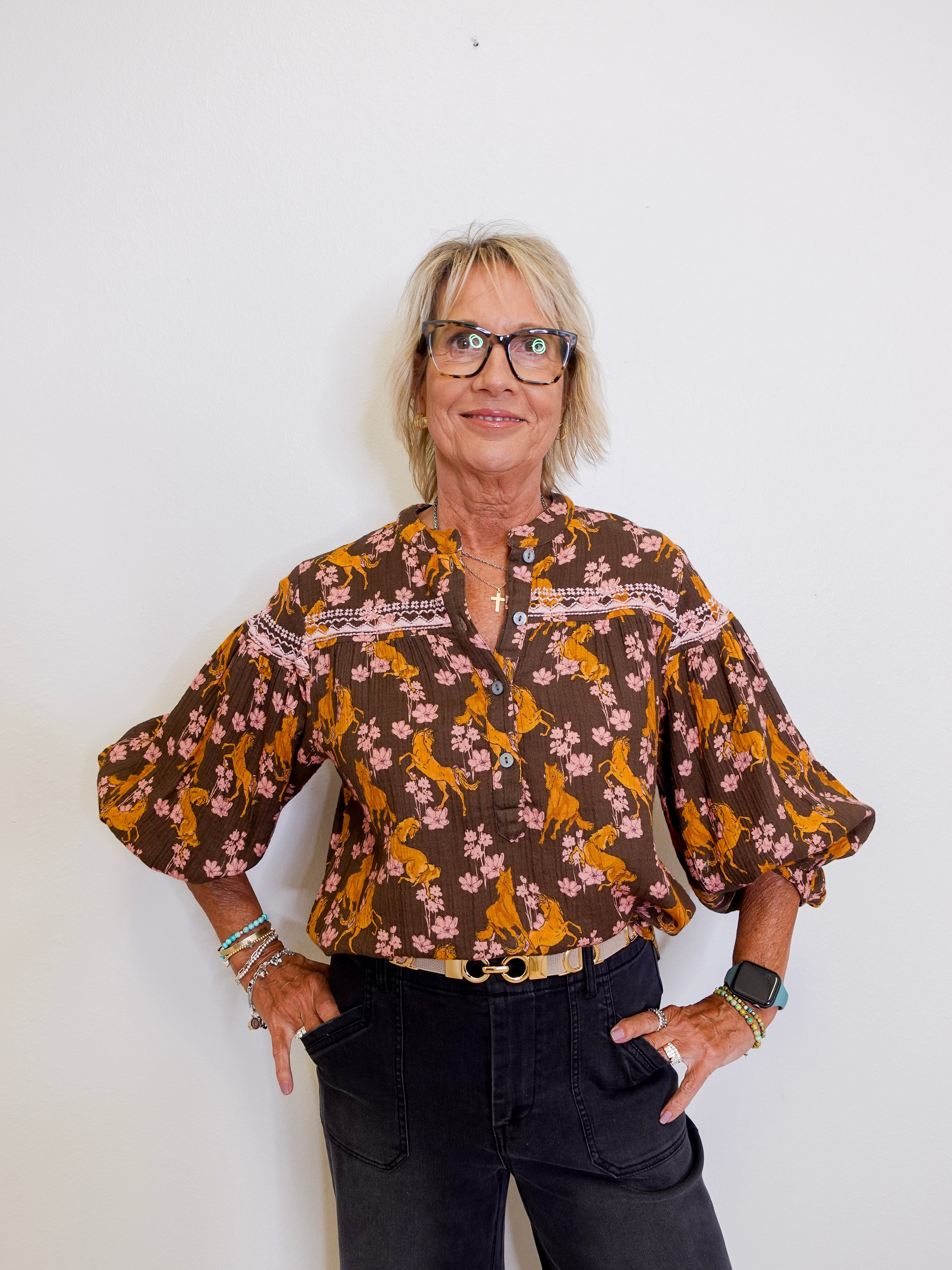 Woman wearing a patterned blouse and black pants against a white background