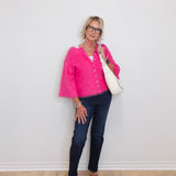 Woman wearing a pink cardigan, blue jeans, and black shoes against a white wall.