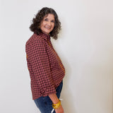 Woman wearing a red plaid shirt and blue jeans against a white wall