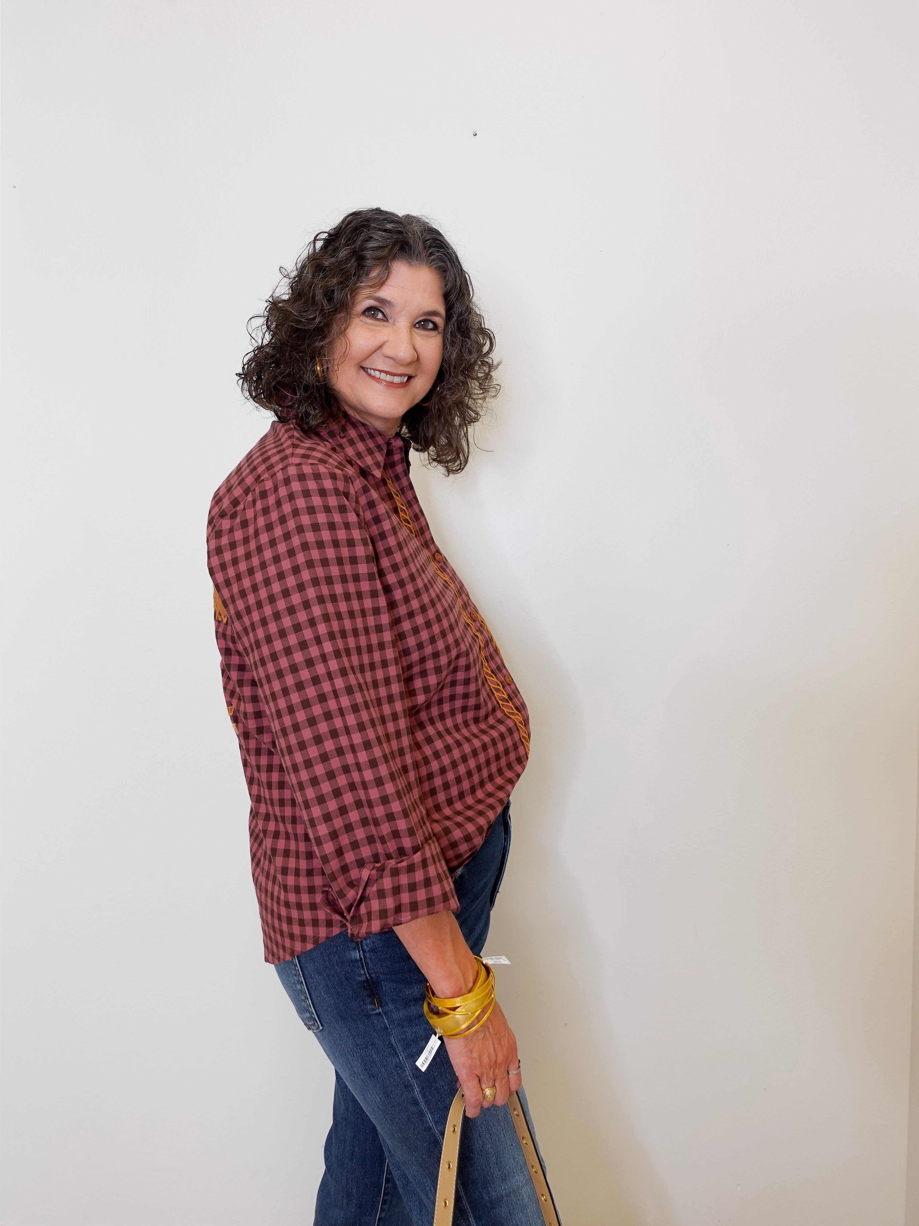 Woman wearing a red plaid shirt and blue jeans against a white wall