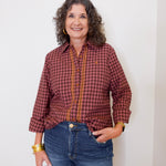 Woman wearing a red plaid shirt and blue jeans against a white wall