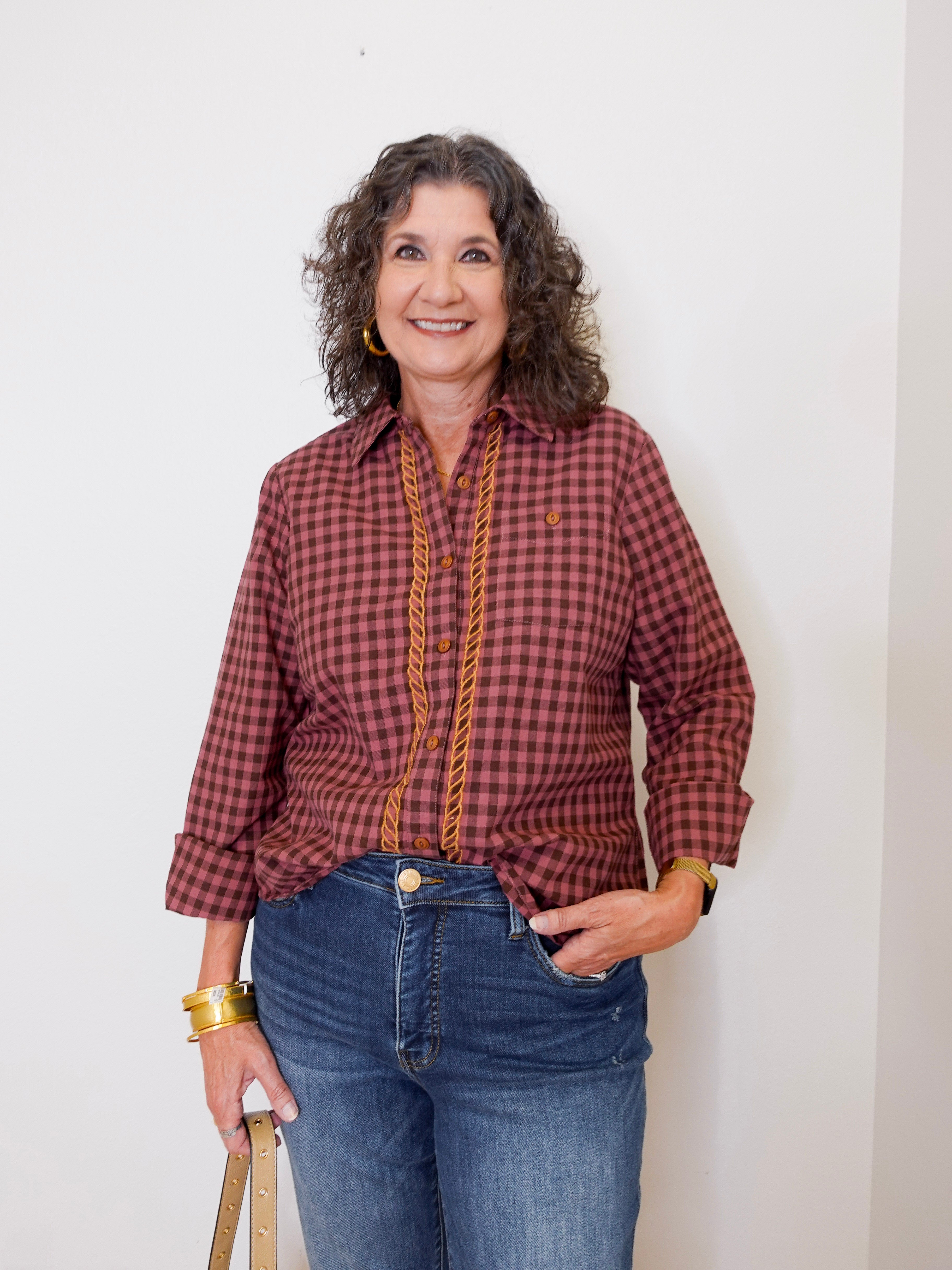 Woman wearing a red plaid shirt and blue jeans against a white wall