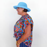Woman wearing a colorful patterned shirt and blue hat against a white background