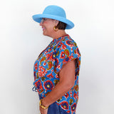Woman wearing a colorful patterned shirt and blue hat against a white background