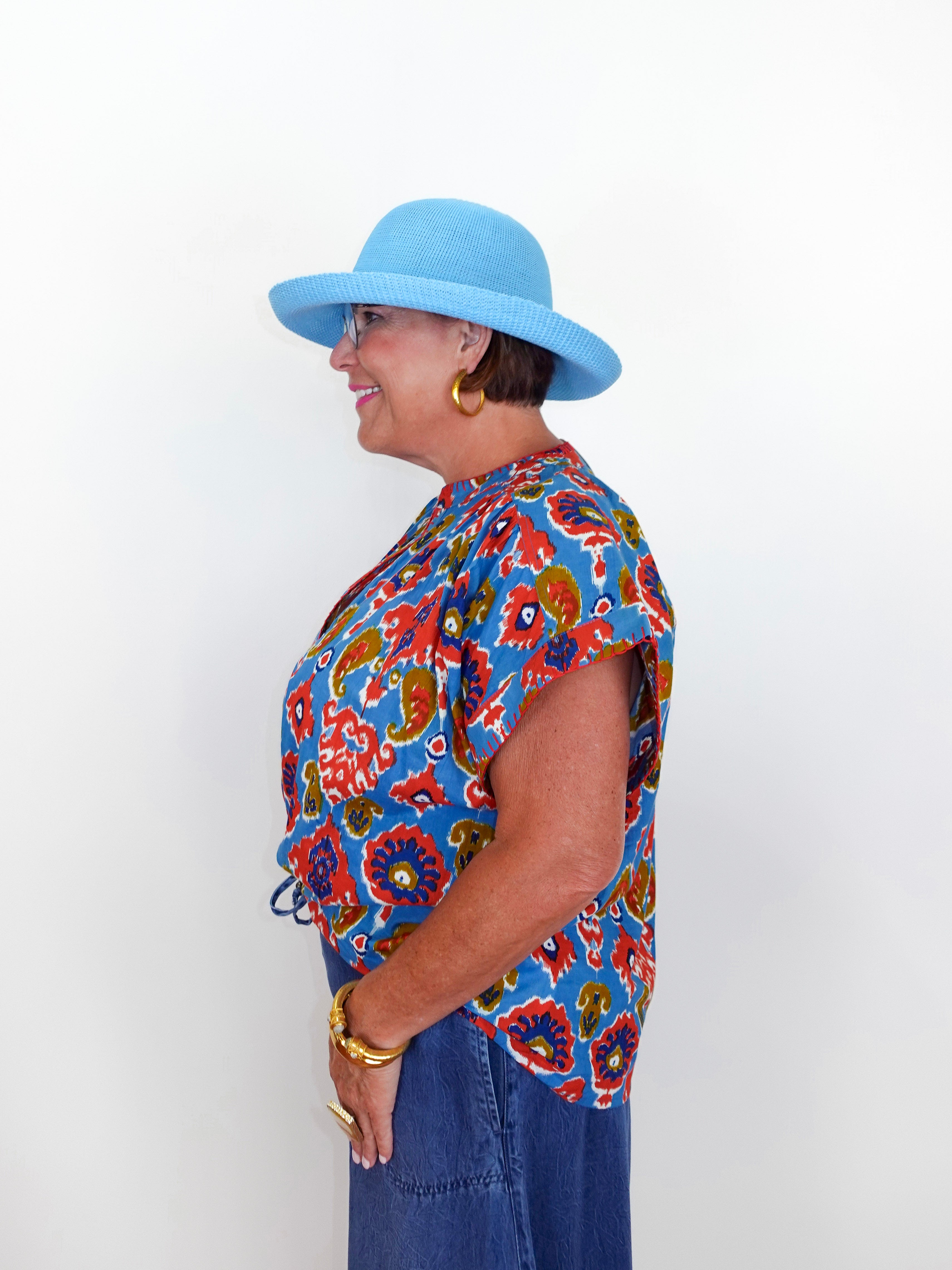 Woman wearing a colorful patterned shirt and blue hat against a white background