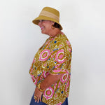 Woman wearing a patterned shirt and hat against a white background