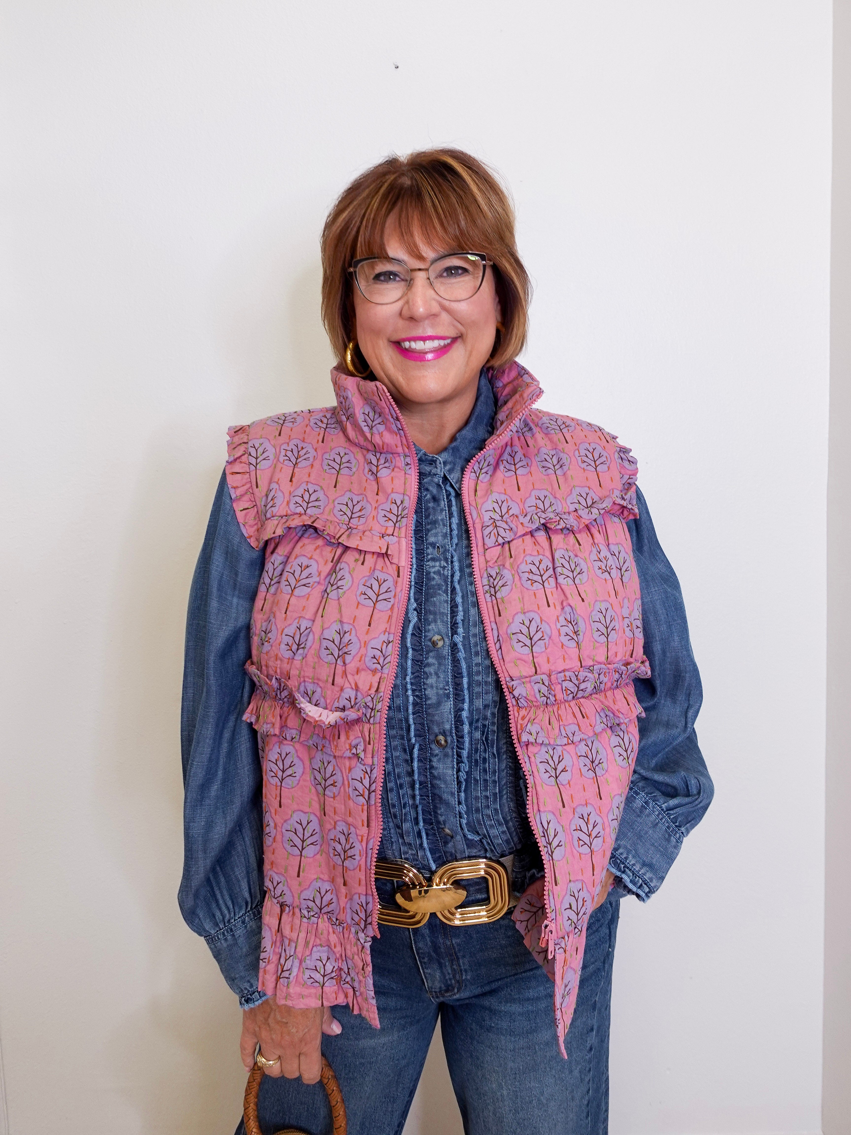 Woman wearing a floral patterned vest over a denim shirt against a plain background