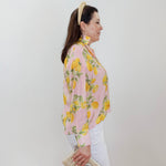 Woman wearing a pink floral blouse with white pants against a plain background