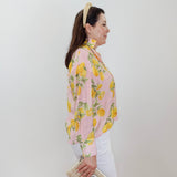 Woman wearing a pink floral blouse with white pants against a plain background