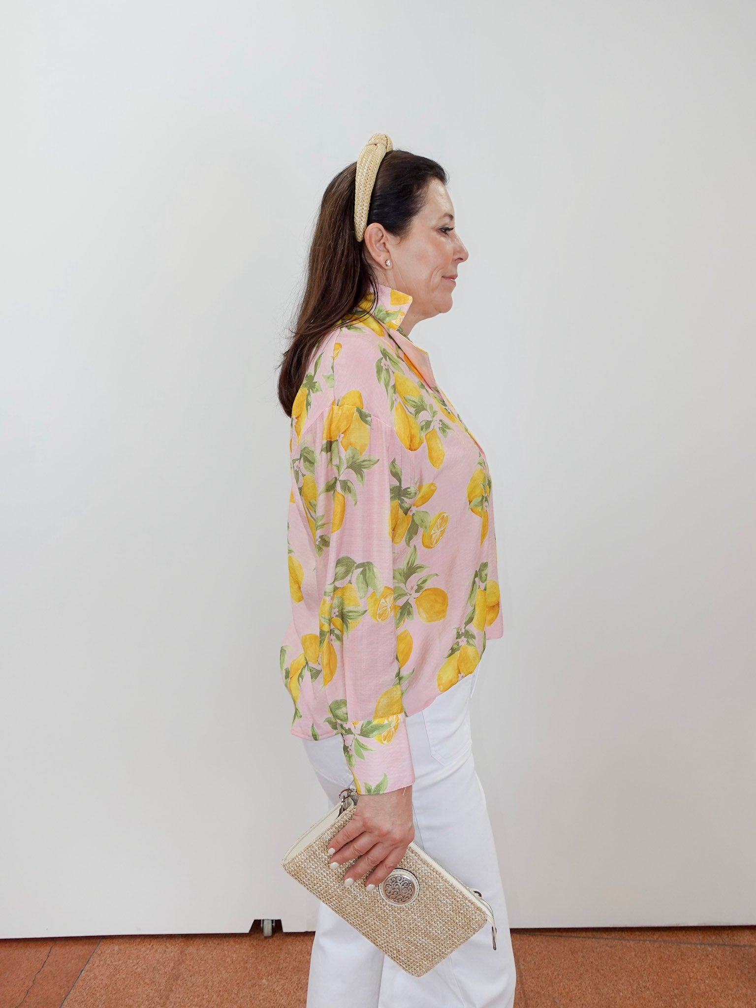 Woman wearing a pink floral blouse with white pants against a plain background