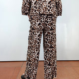 A person shown from the back wearing a matching leopard-print pajama set with a long-sleeve top and wide-leg pants, paired with black platform sandals, against a white wall and terracotta tiled floor.