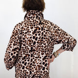 A person shown from the back wearing a leopard print long-sleeve top or jumpsuit against a plain white wall.