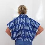 Person wearing a blue shirt with white patterns on a plain background