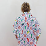 Person wearing a colorful patterned shirt with red pants on a plain background