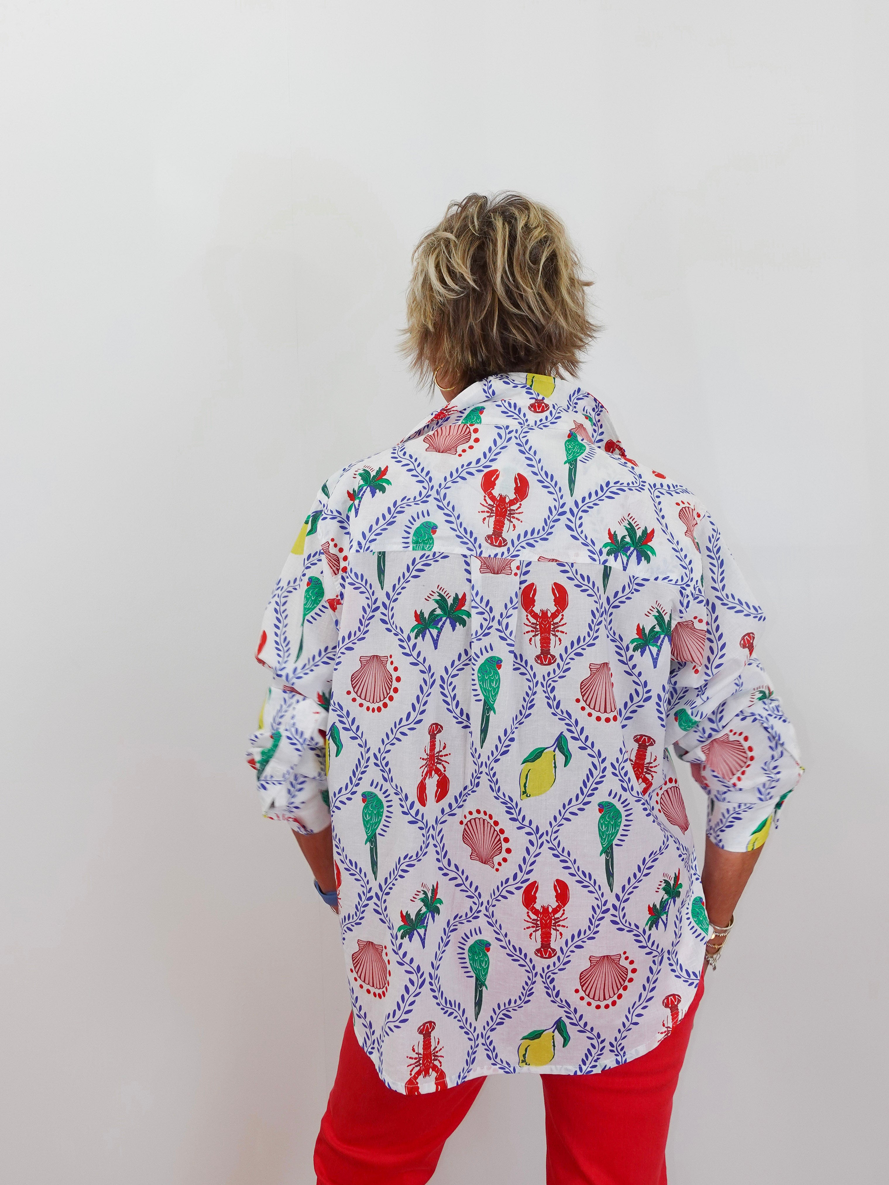 Person wearing a colorful patterned shirt with red pants on a plain background