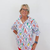 Woman wearing a colorful patterned shirt with red pants on a white background