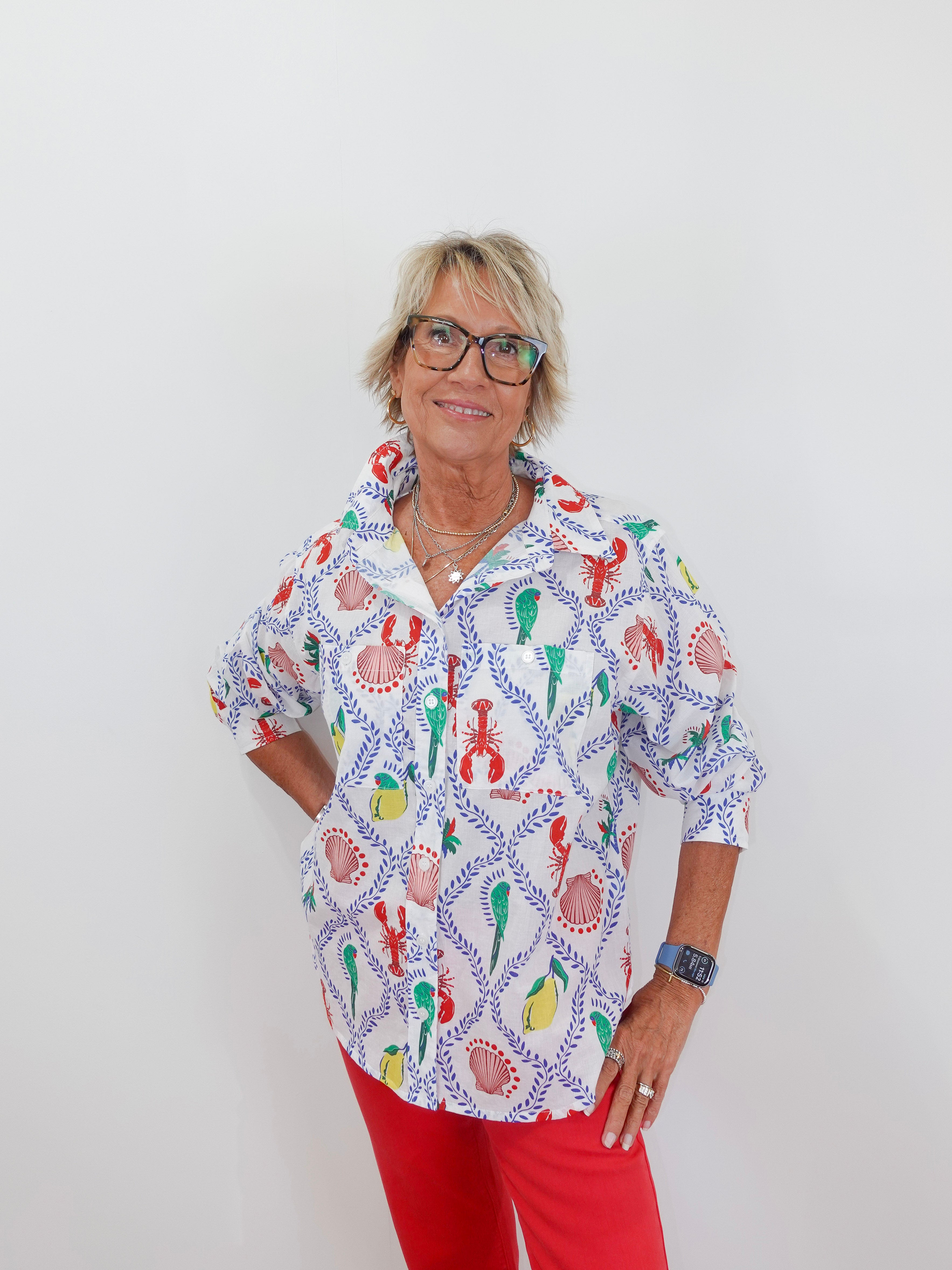 Woman wearing a colorful patterned shirt with red pants on a white background
