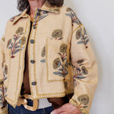 Woman wearing a beige embroidered jacket against a white background